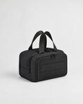 A black nylon toiletry bag with dual top handles, a zippered main compartment, and a front zippered pocket, shown on a light gray studio background.